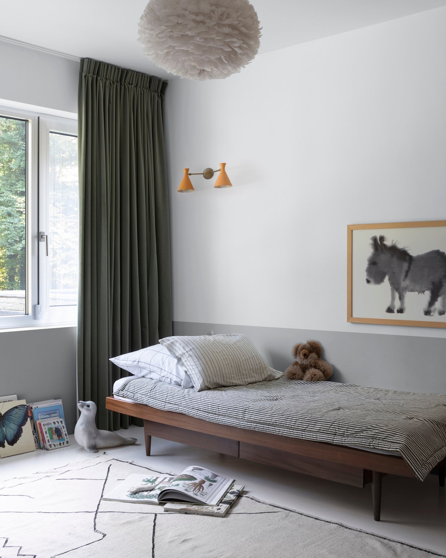 Chambre d’enfant aux murs blanc lingère Libéron et soubassement gris fer blanc, avec lit en bois et rideaux vert foncé.