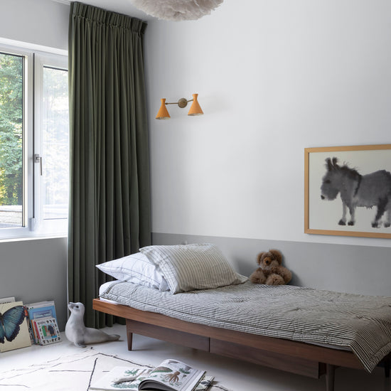 Chambre d’enfant aux murs blanc lingère Libéron et soubassement gris fer blanc, avec lit en bois et rideaux vert foncé.