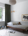 Chambre d’enfant aux murs blanc lingère Libéron et soubassement gris fer blanc, avec lit en bois et rideaux vert foncé.
