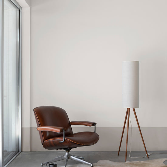 Salon épuré aux murs blanc mousseline et soubassement grège tapissier Libéron, avec fauteuil cuir et lampe sur pied.