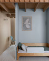 Chambre aux murs 163 Faubourg bleu couture et beige bottier Libéron, avec lit en bois, poutres apparentes et chaise bleue.