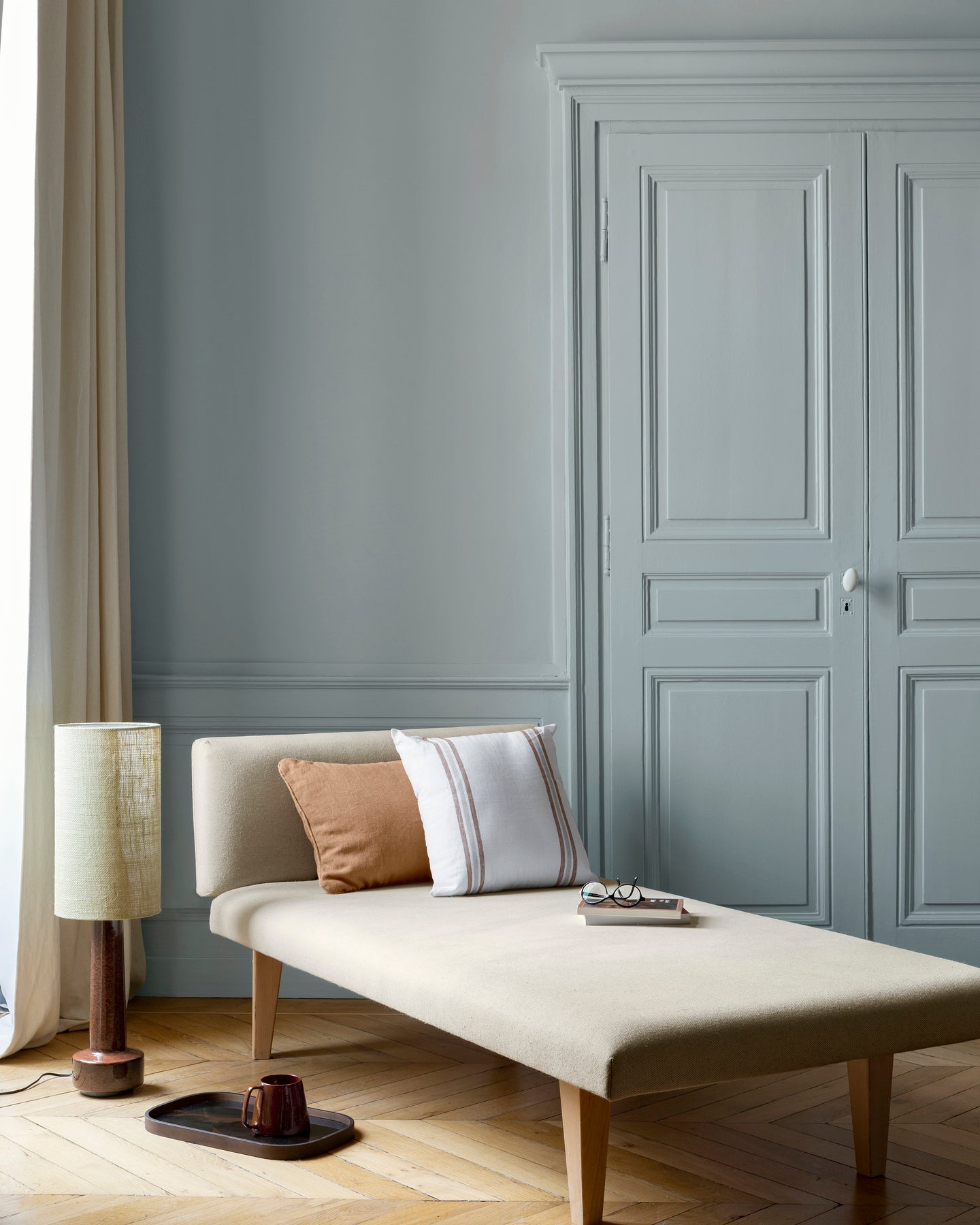 Salon aux murs bleu couture Libéron, avec méridienne écrue, portes assorties, coussins terracotta et parquet clair.