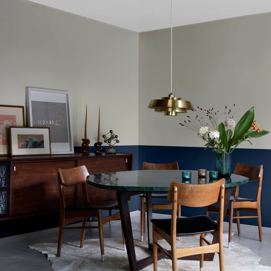 Salle à manger aux murs 163 Faubourg bleu maritime et lait d’amande Libéron, avec table ronde, chaises en bois et buffet vintage.
