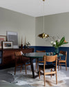 Salle à manger aux murs 163 Faubourg bleu maritime et lait d’amande Libéron, avec table ronde, chaises en bois et buffet vintage.