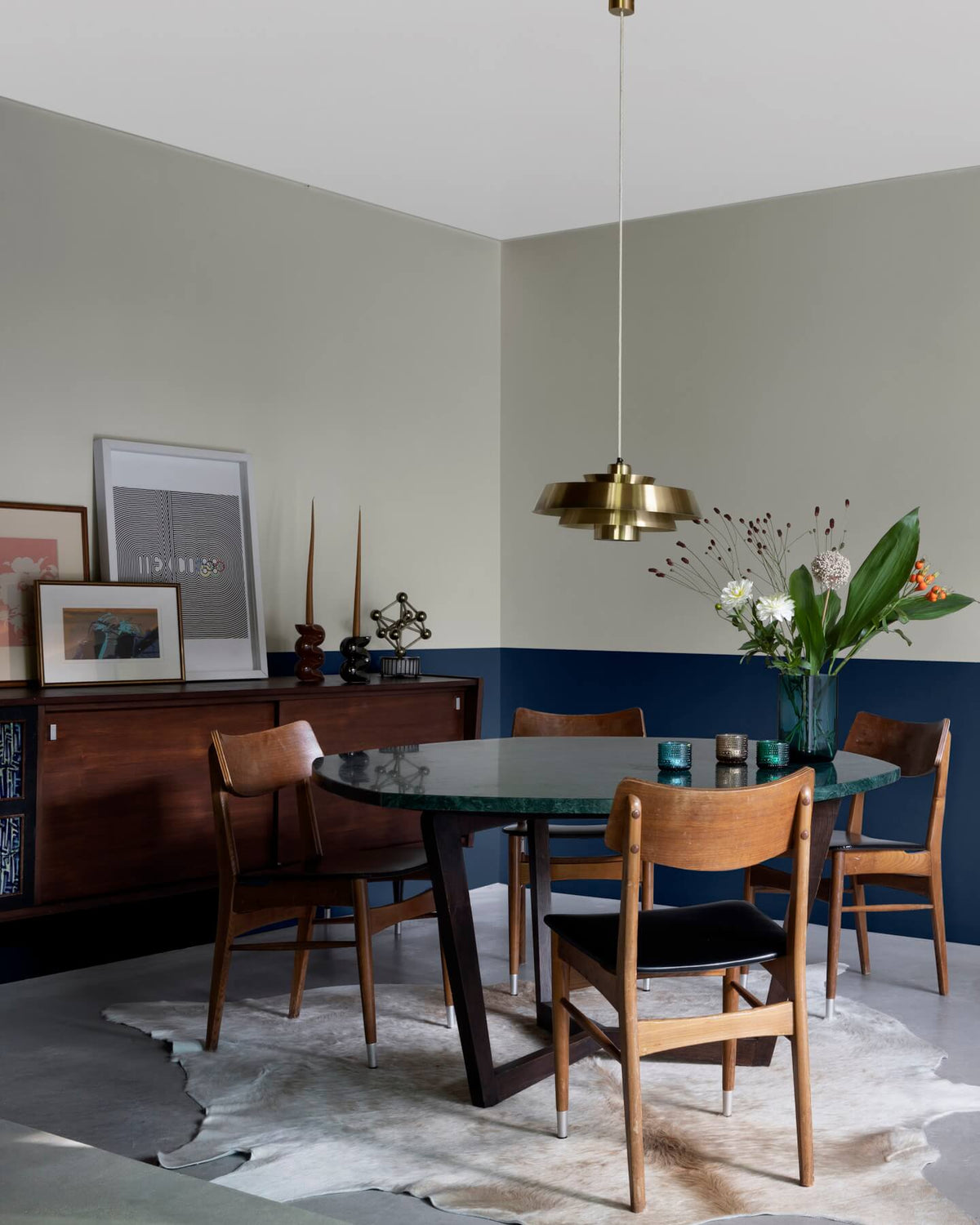 Salle à manger aux murs 163 Faubourg bleu maritime et lait d’amande Libéron, avec table ronde, chaises en bois et buffet vintage.