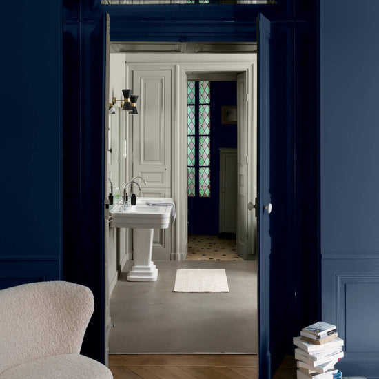 Passage aux murs 163 Faubourg bleu maritime et lait d’amande Libéron, avec fauteuil crème, portes bleues et lavabo blanc.