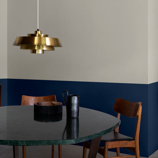 Salle à manger aux murs 163 Faubourg bleu maritime et lait d’amande Libéron, avec table sombre, chaises en bois et suspension dorée.