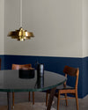 Salle à manger aux murs 163 Faubourg bleu maritime et lait d’amande Libéron, avec table sombre, chaises en bois et suspension dorée.