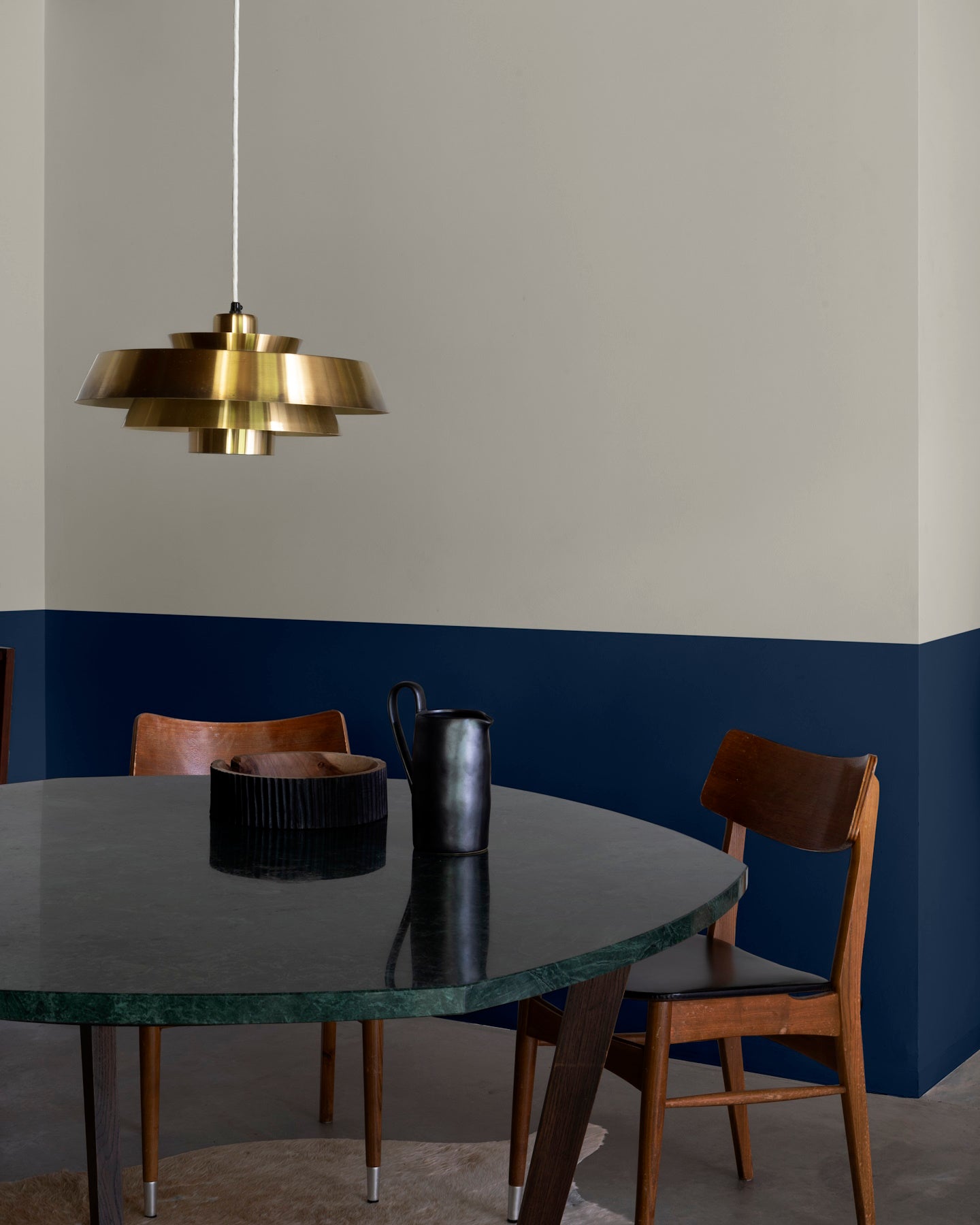 Salle à manger aux murs 163 Faubourg bleu maritime et lait d’amande Libéron, avec table sombre, chaises en bois et suspension dorée.