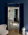 Ouverture bleu maritime Libéron sur salle de bain lait d’amande, avec fauteuil crème, livres et parquet en chevrons.