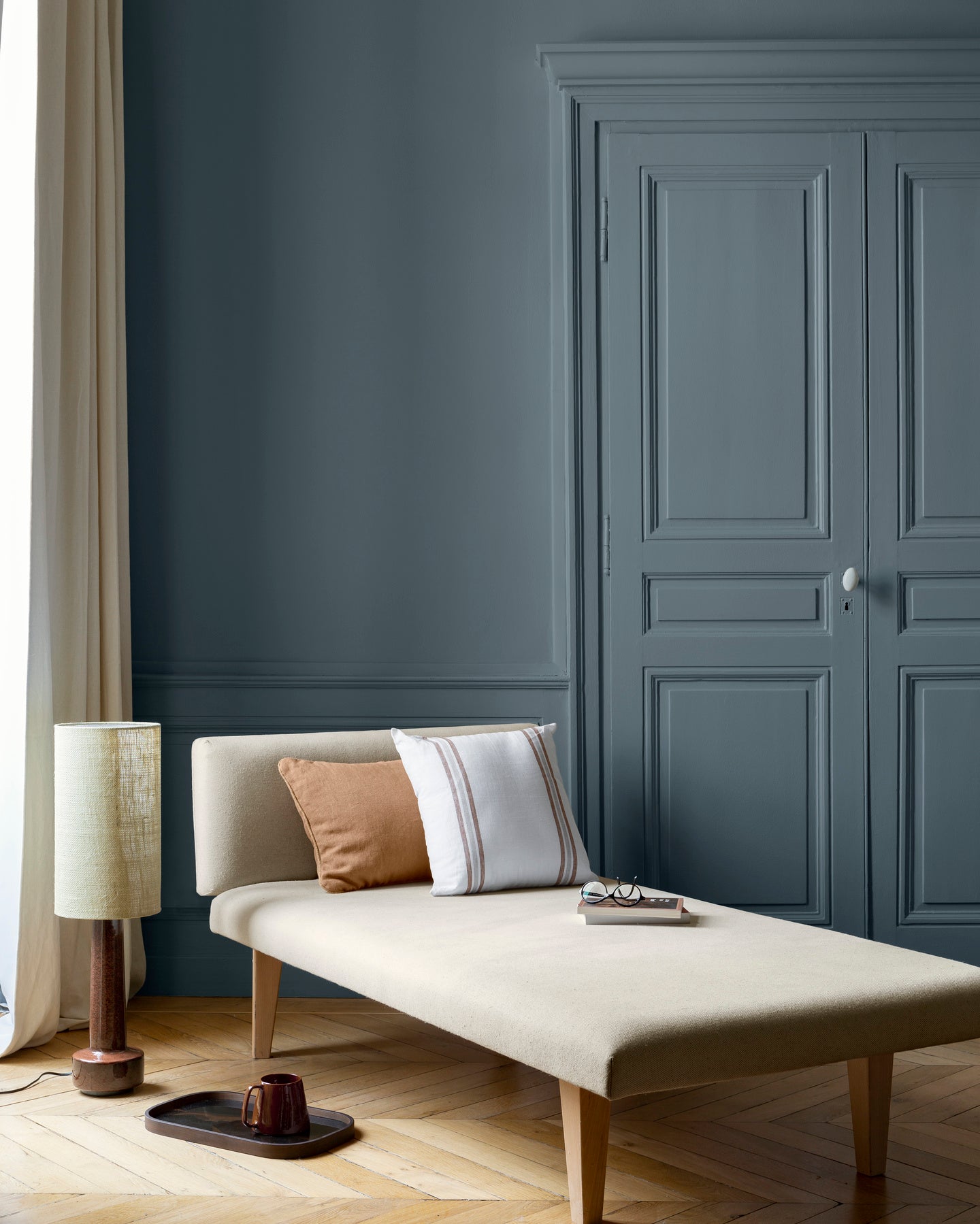 Salon aux murs bleu zingueur Libéron, avec méridienne écrue, portes assorties, coussins terracotta et parquet clair.