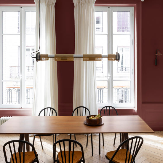 Salle à manger lumineuse avec murs rouges, peinture 163 Faubourg Bordeaux Tomette Libéron, avec rideaux blancs, table et chaises en bois