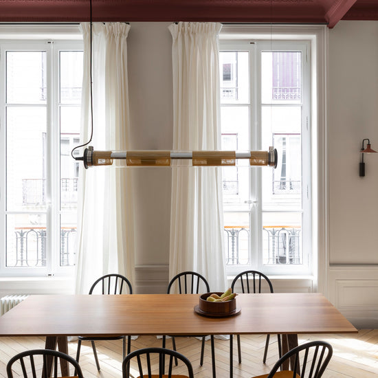 Salle à manger Libéron avec plafond bordeaux tomette, murs grège tapissier, grande table en bois et rideaux blancs.