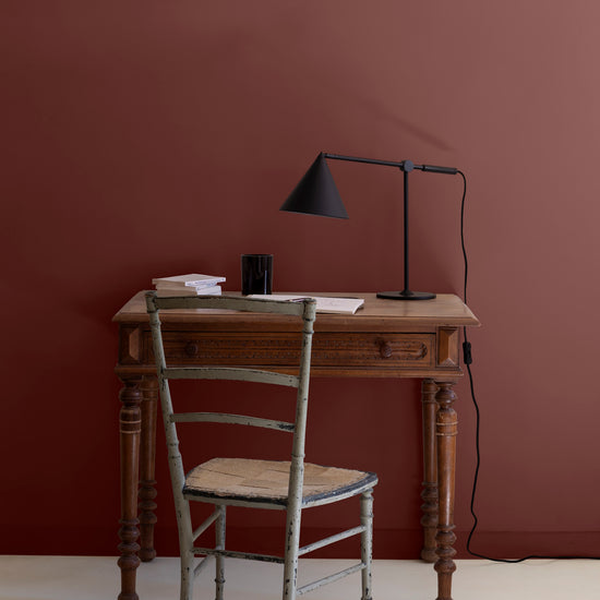 Bureau en bois devant un mur bordeaux tomette et ivoire orfèvre Libéron, avec chaise ancienne et lampe noire.