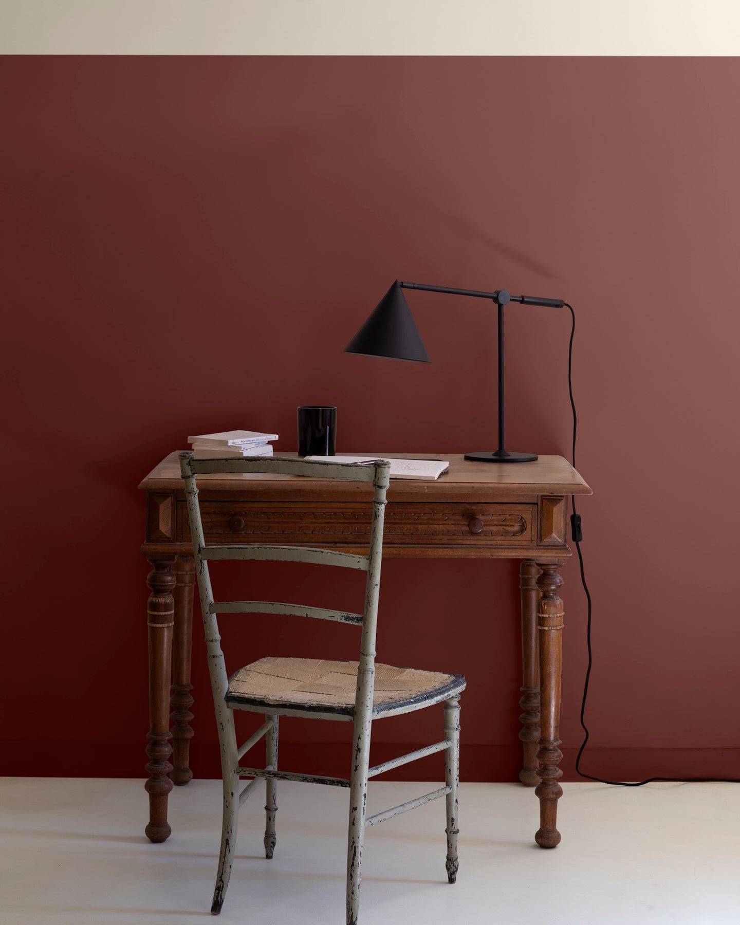 Bureau en bois devant un mur bordeaux tomette et ivoire orfèvre Libéron, avec chaise ancienne et lampe noire.