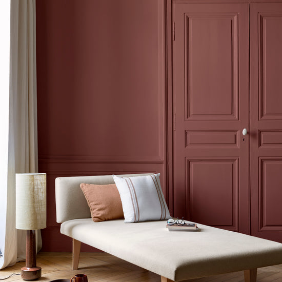 Salon aux murs bordeaux tomette Libéron, avec méridienne écrue, portes assorties, coussins terracotta et parquet clair.