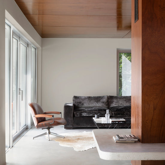 Salon aux murs grège tapissier Libéron, avec plafond et cloison en bois, canapé sombre et baie vitrée.