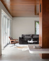 Salon aux murs grège tapissier Libéron, avec plafond et cloison en bois, canapé sombre et baie vitrée.