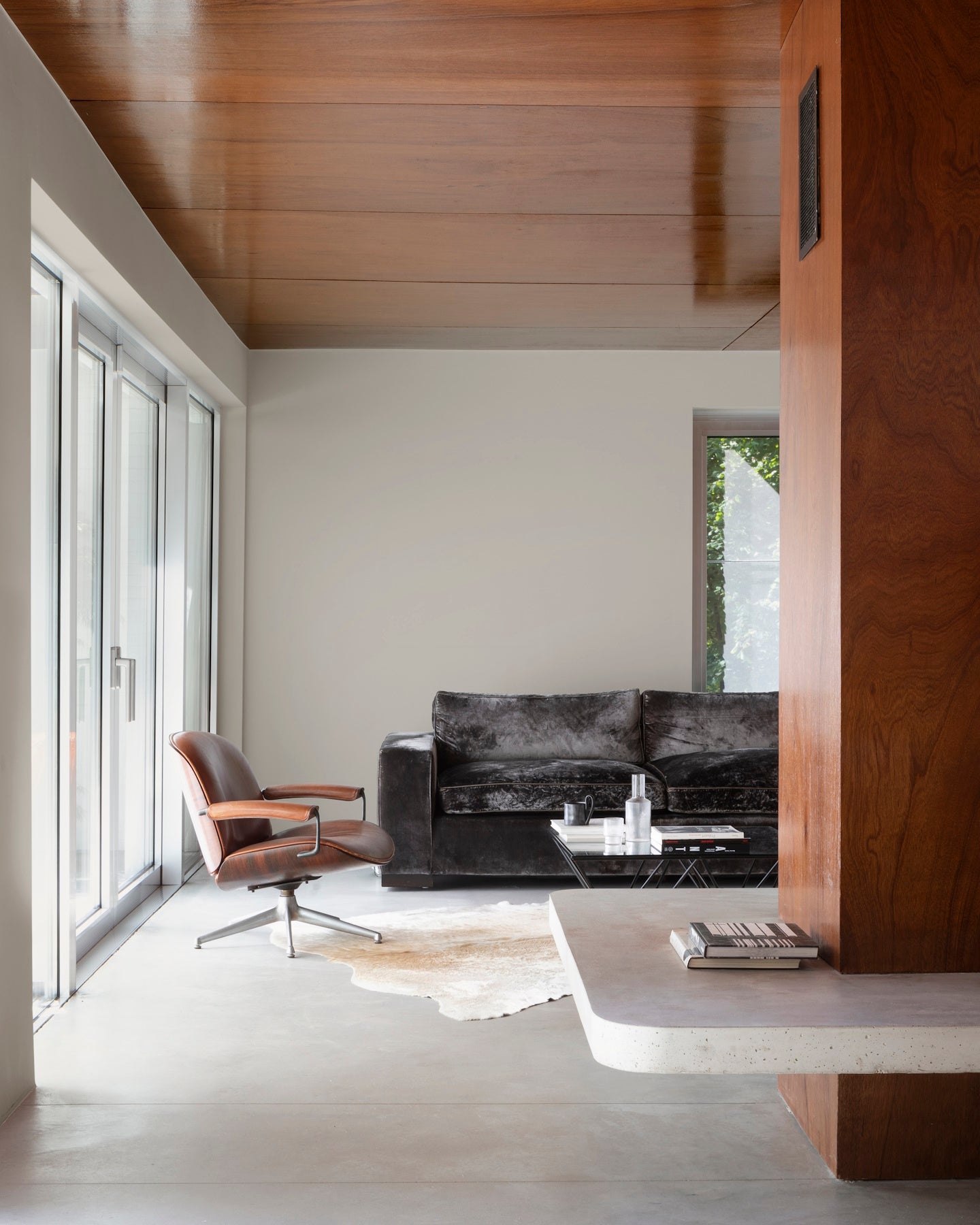 Salon aux murs grège tapissier Libéron, avec plafond et cloison en bois, canapé sombre et baie vitrée.