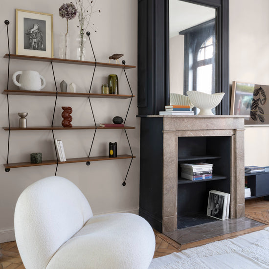 Salon aux murs grège tapissier Libéron, avec étagères murales, cheminée noire et fauteuil blanc sculptural.