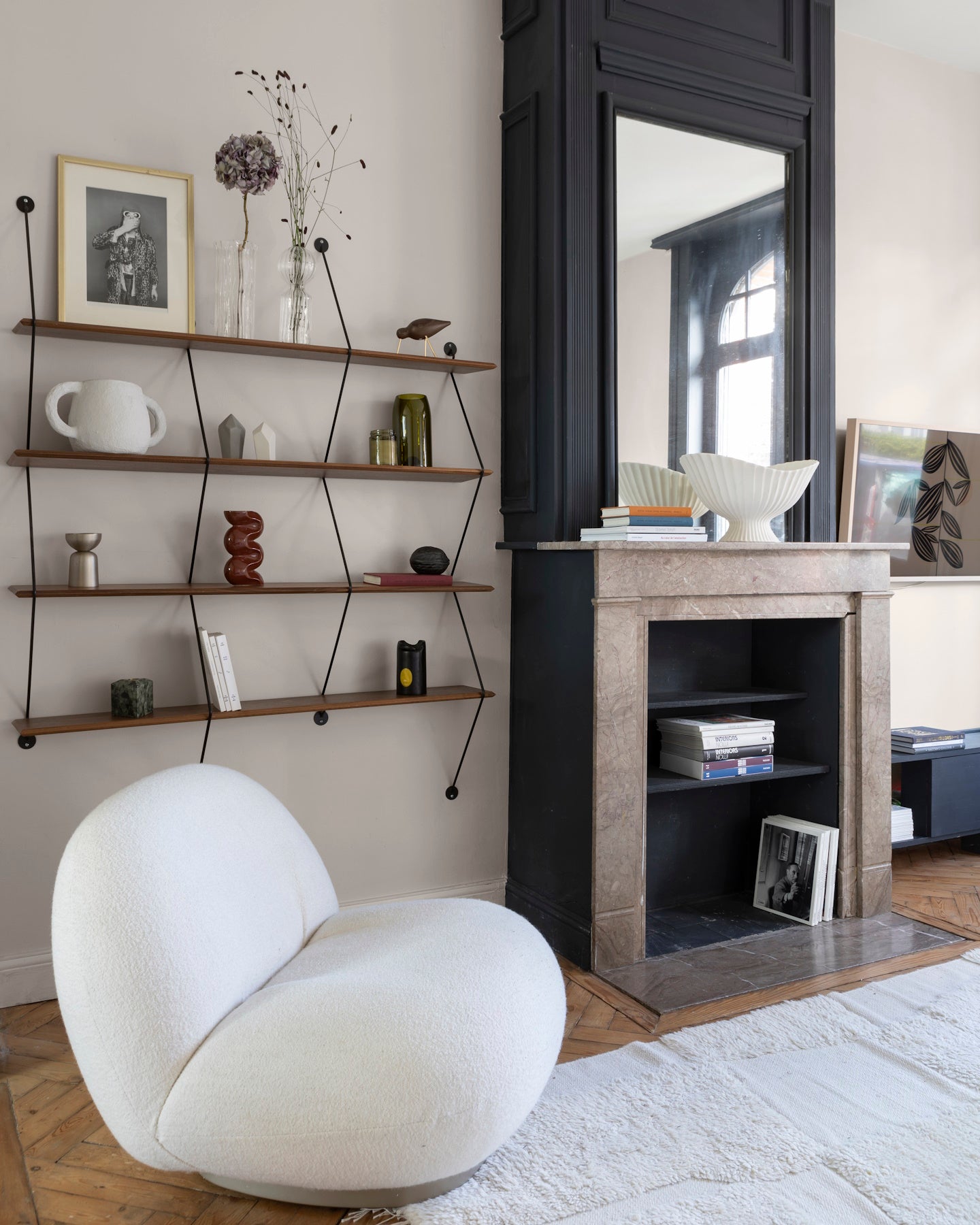 Salon aux murs grège tapissier Libéron, avec étagères murales, cheminée noire et fauteuil blanc sculptural.