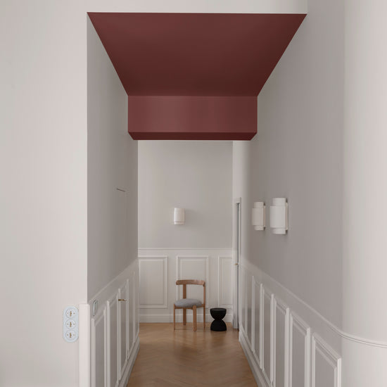Couloir aux murs grège tapissier Libéron, soubassement blanc et plafond bordeaux tomette, avec parquet en chevrons.