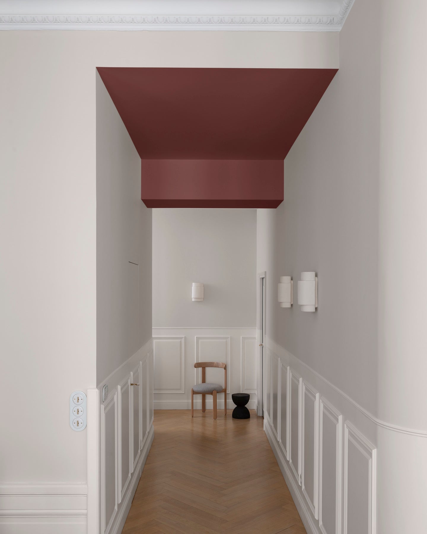 Couloir aux murs grège tapissier Libéron, soubassement blanc et plafond bordeaux tomette, avec parquet en chevrons.