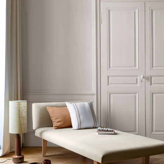 Salon aux murs grège tapissier Libéron, avec méridienne écrue, portes assorties, coussins terracotta et parquet clair.