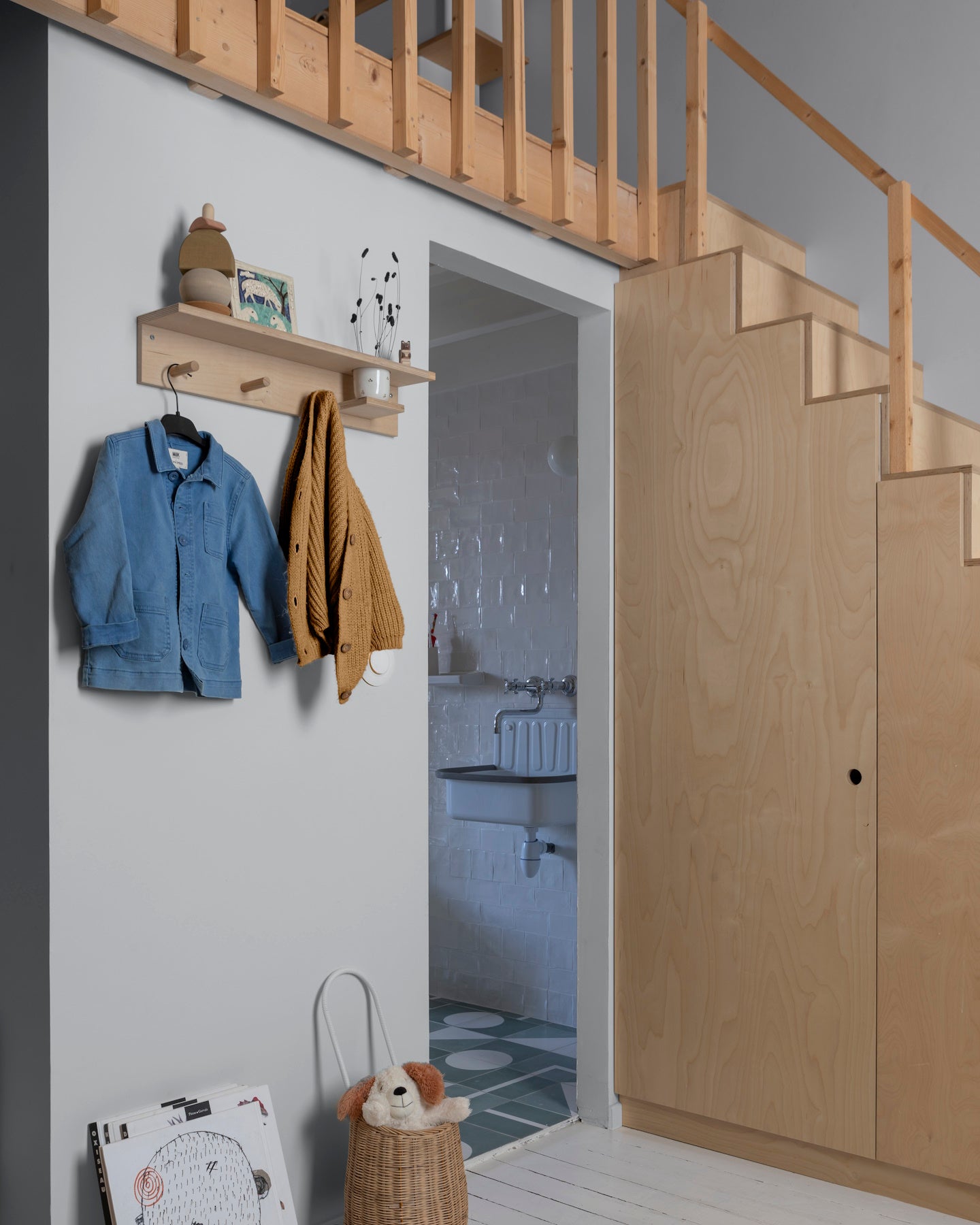 Entrée gris fer blanc Libéron avec escalier en bois clair, patères murales et coin salle de bain.