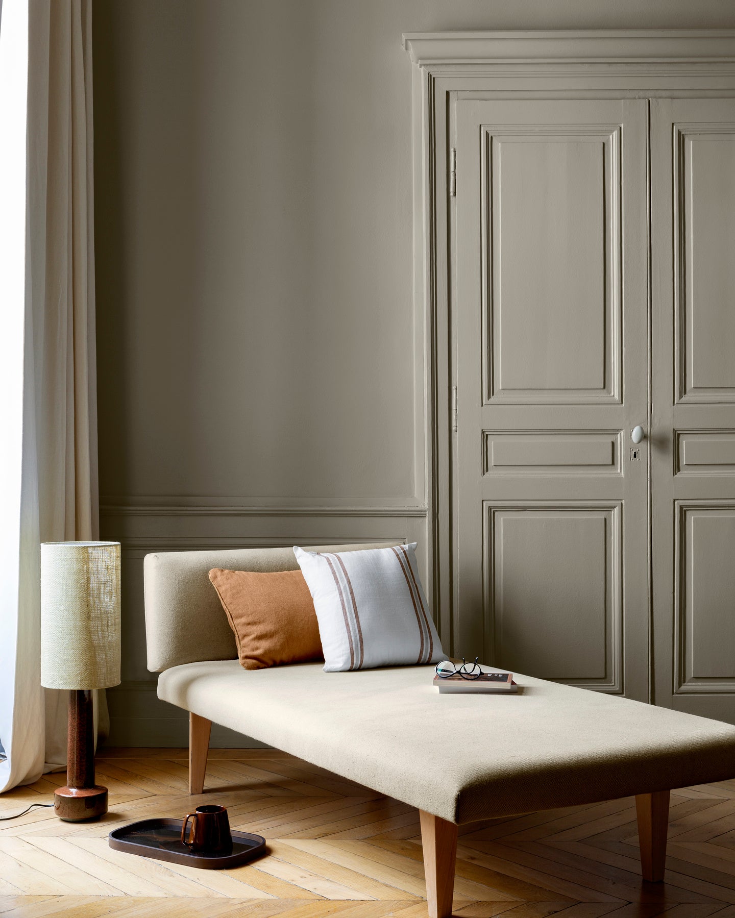 Salon aux murs Gris Grande Dame 163 Faubourg Libéron, avec méridienne écrue, portes assorties et parquet clair.