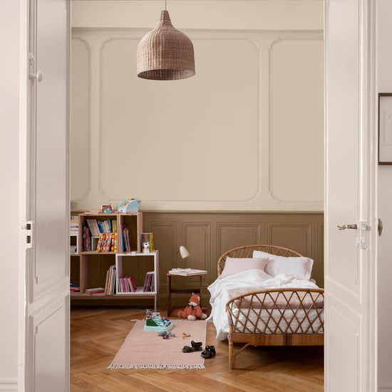 Chambre d’enfant aux murs ivoire orfèvre et soubassement beige bottier Libéron, avec lit en rotin, bibliothèque et parquet.