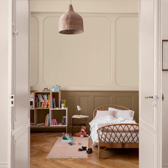 Chambre d’enfant aux murs ivoire orfèvre et soubassement beige bottier Libéron, avec lit en rotin, bibliothèque et parquet.