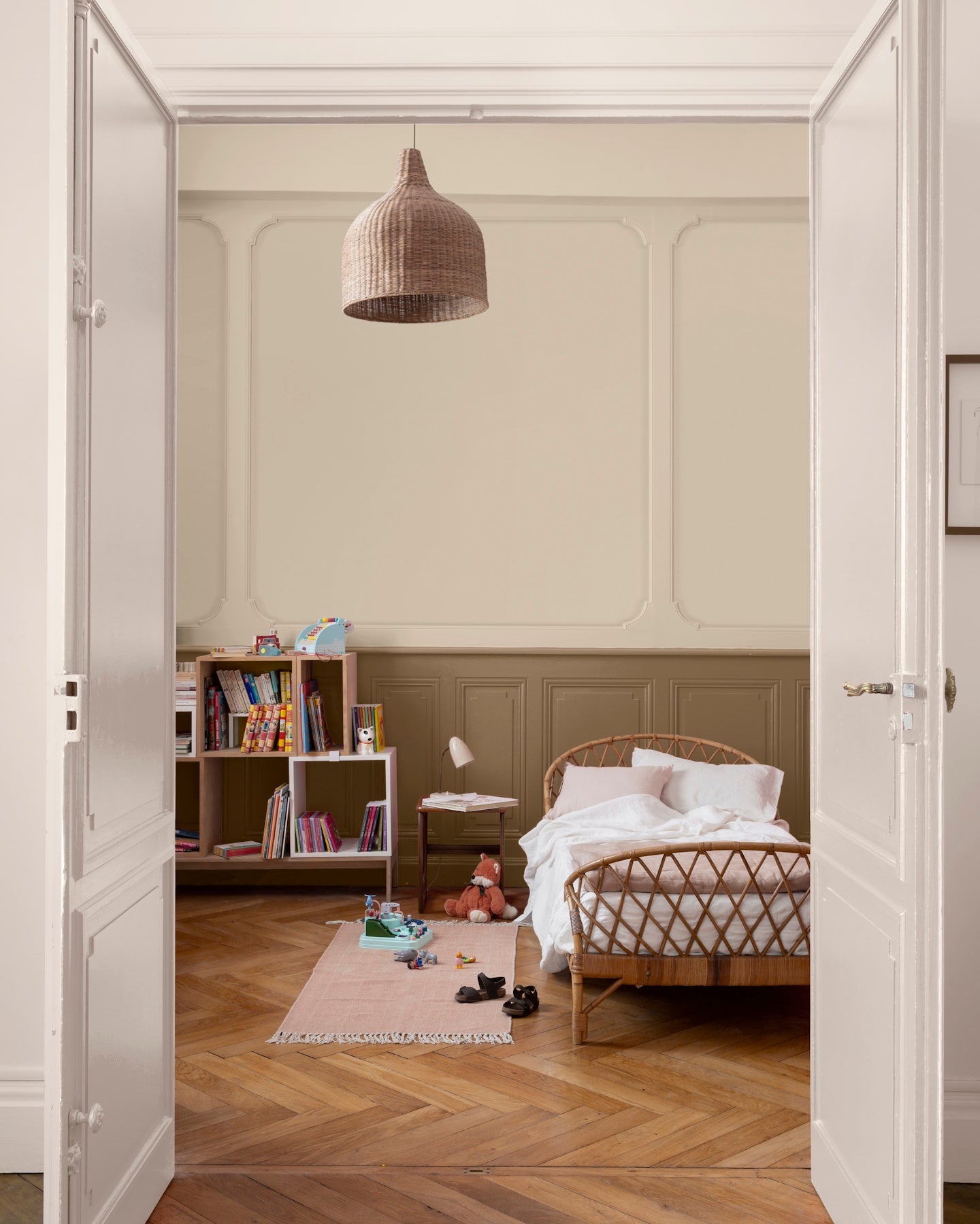 Chambre d’enfant aux murs ivoire orfèvre et soubassement beige bottier Libéron, avec lit en rotin, bibliothèque et parquet.