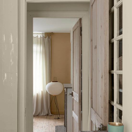 Enfilade de portes en bois clair sur murs ivoire orfèvre et beige bottier Libéron, avec rideaux en lin et lampe blanche.