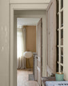 Enfilade de portes en bois clair sur murs ivoire orfèvre et beige bottier Libéron, avec rideaux en lin et lampe blanche.