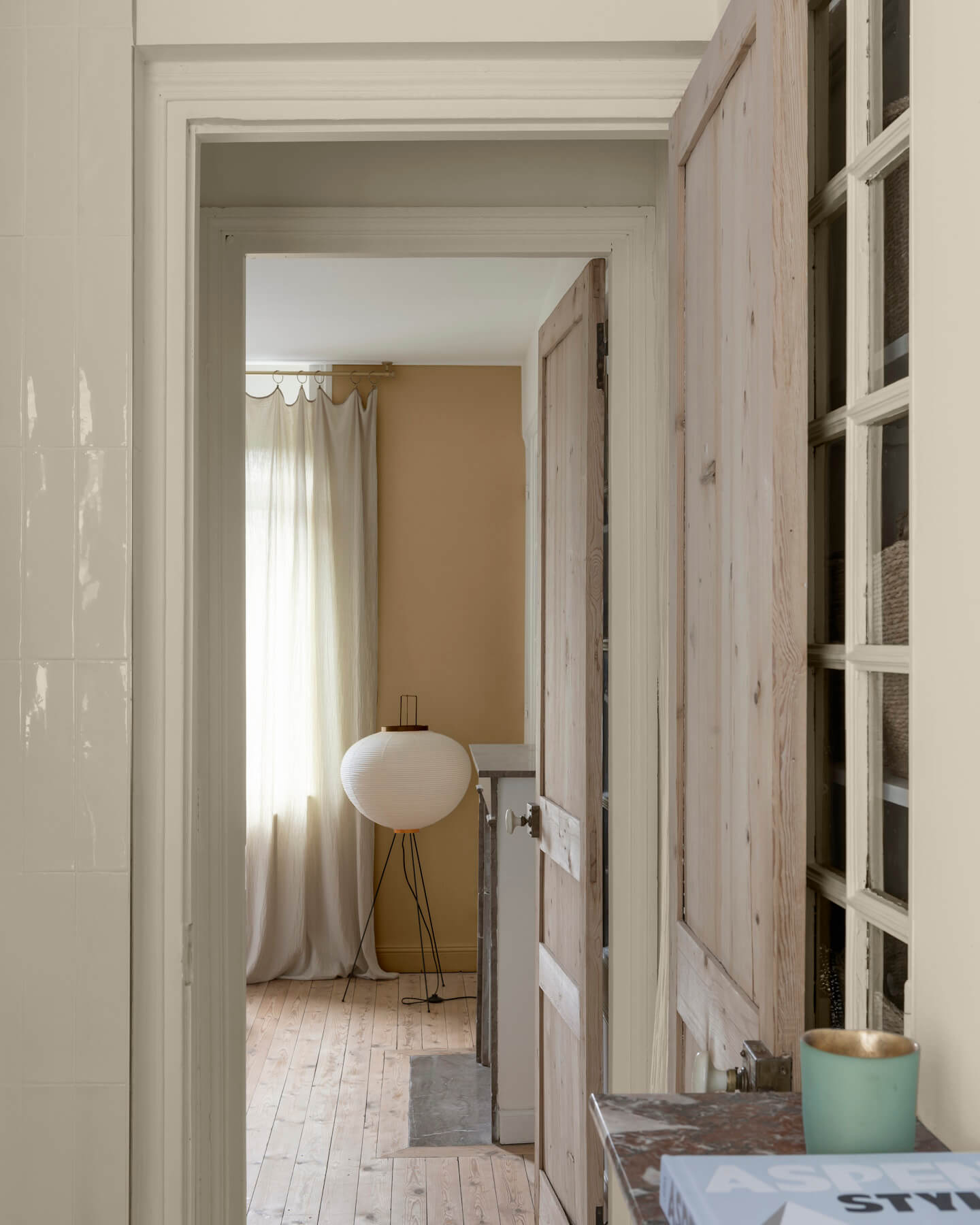 Enfilade de portes en bois clair sur murs ivoire orfèvre et beige bottier Libéron, avec rideaux en lin et lampe blanche.