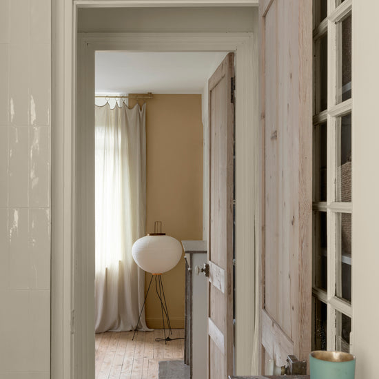 Enfilade de portes en bois clair sur murs ivoire orfèvre et beige bottier Libéron, avec rideaux en lin et lampe blanche.