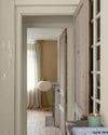 Enfilade de portes en bois clair sur murs ivoire orfèvre et beige bottier Libéron, avec rideaux en lin et lampe blanche.