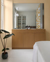 Salle de bain aux murs jaune tesselle Libéron, avec meuble vasque en bois clair, grand miroir et plante verte.