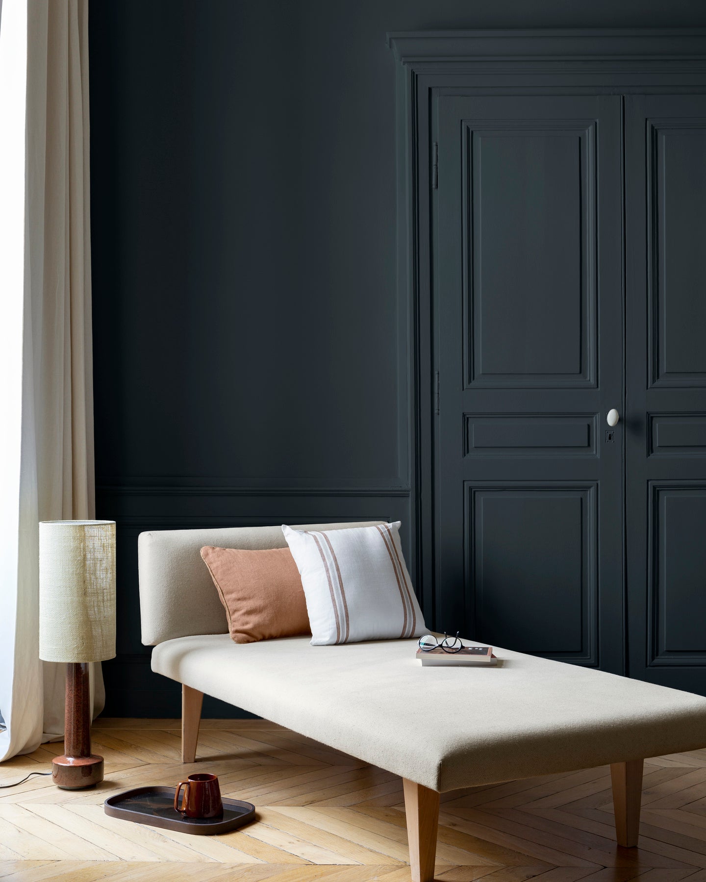 Salon lumineux avec porte et murs noirs, peinture 163 Faubourg Noir d'Imprimerie Libéron, avec méridienne blanche
