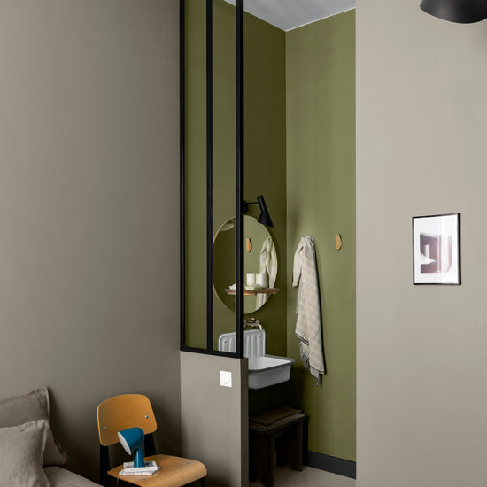 Coin chambre et salle d’eau aux murs vert botanique et gris grande dame Libéron, avec verrière noire et chaise bois.