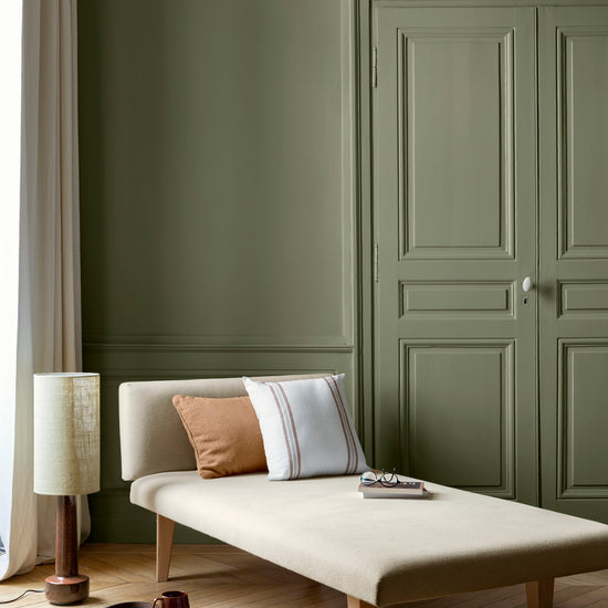 Salon aux murs Vert Ombrelle Libéron, avec méridienne écrue, portes assorties, coussins terracotta et parquet clair.