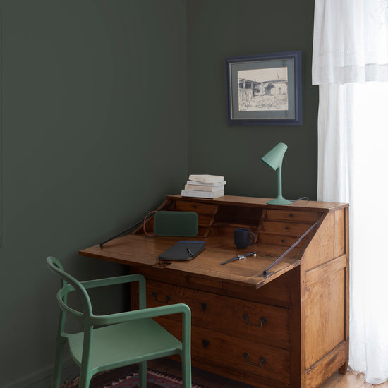 Coin bureau teint avec La Teinte Antiquaire Merisier Libéron, chaise, lampe et murs verts, et cadre accroché au mur