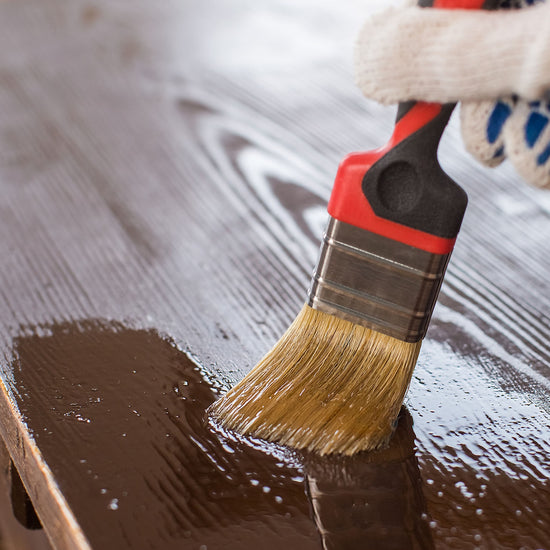 Main appliquant le Traitement Meubles et Boiseries Libéron au pinceau sur une surface en bois