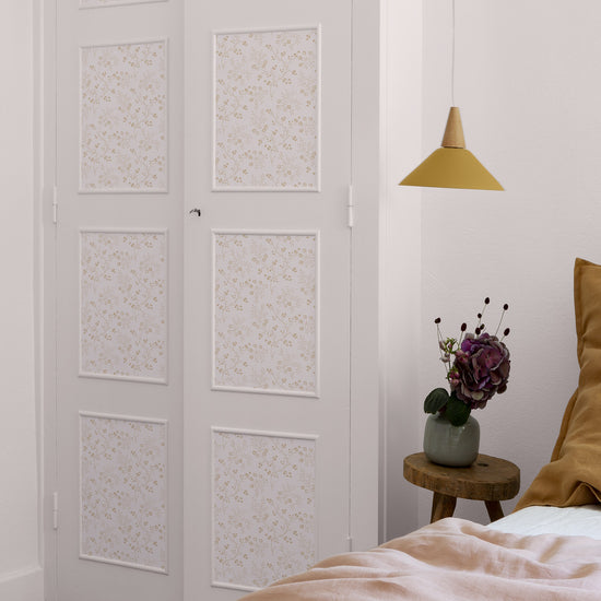 Chambre aux tons poudrés avec porte fleurie Libéron Belle Jeanne, linge rose pâle et coussins ocre.