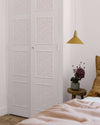 Chambre aux tons poudrés avec porte fleurie Libéron Belle Jeanne, linge rose pâle et coussins ocre.