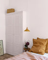 Chambre aux murs rose poudré, avec armoire blanche à panneaux floraux Belle Jeanne Libéron, suspension ocre et linge de lit rose.