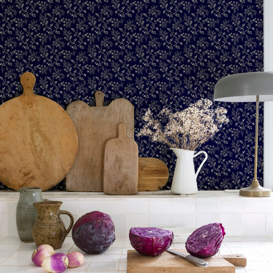 Cuisine au mur floral bleu nuit, teinte Belle Jeanne Libéron, avec plan de travail blanc, lampes et légumes violets.