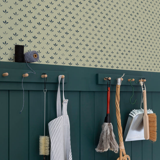 Coin cuisine avec papier peint Velours de Papier Florette n°3 Libéron, soubassement vert foncé, tablier et outils de nettoyage suspendus sur des accroches murales.