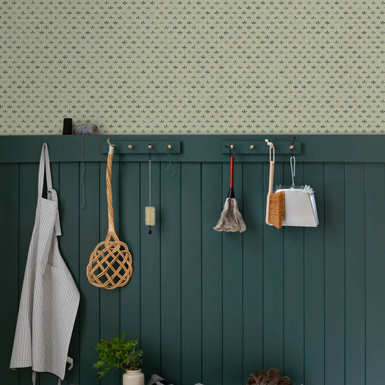Entrée au mur Florette Libéron, avec papier peint crème à petit motif bleu, soubassement vert foncé, banc en bois et patères.